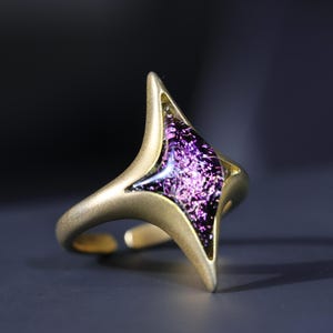 May include: A gold ring featuring a purple, iridescent, glass-like stone in the shape of a star.