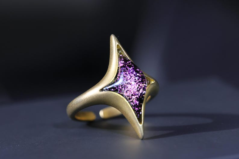 May include: A gold ring featuring a purple, iridescent, glass-like stone in the shape of a star.