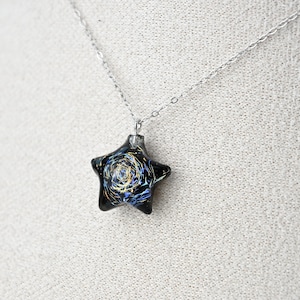 May include: A silver chain necklace with a black star-shaped pendant. The pendant has a swirling blue and gold design inside.