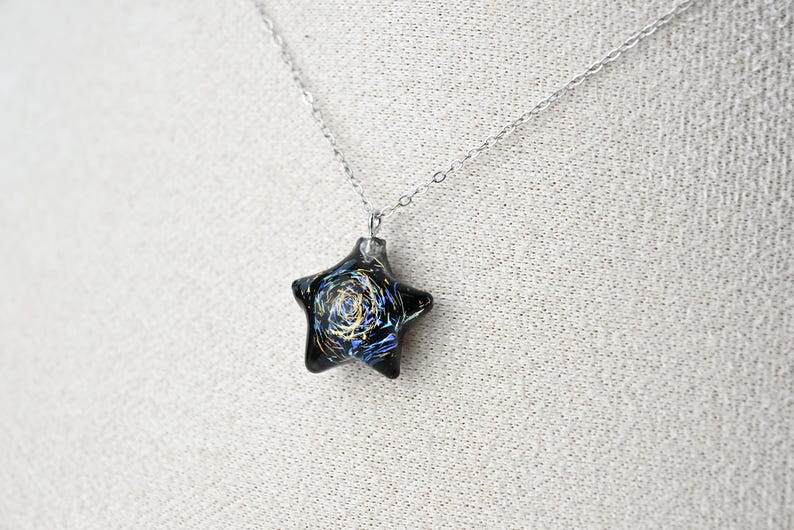 May include: A silver chain necklace with a black star-shaped pendant. The pendant has a swirling blue and gold design inside.