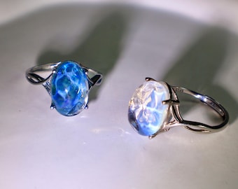 May include: Two silver rings with oval-shaped blue and white iridescent stones. The rings have a delicate design.