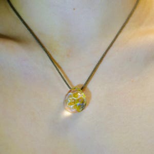Puede incluir: Un collar delicado con un colgante de vidrio transparente con un dise&ntilde;o floral amarillo.