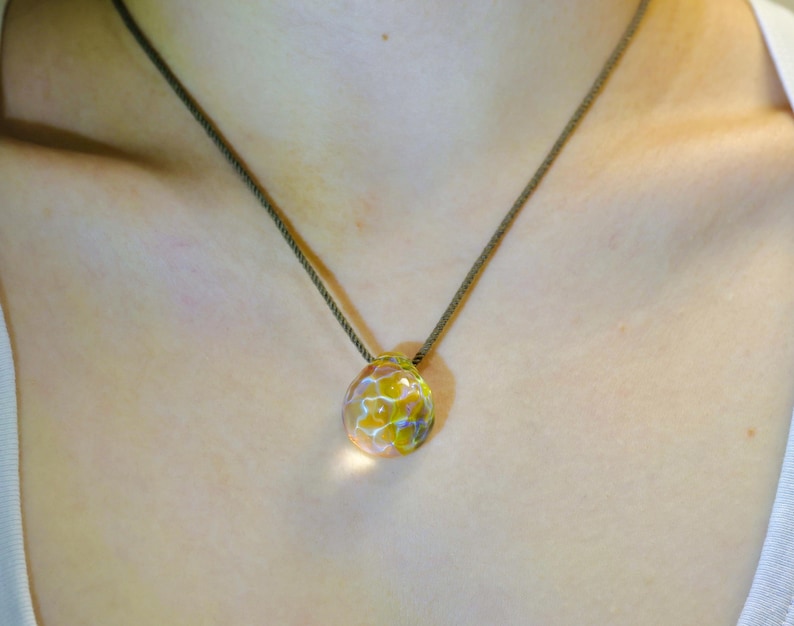 Puede incluir: Un collar delicado con un colgante de vidrio transparente con un dise&ntilde;o floral amarillo.