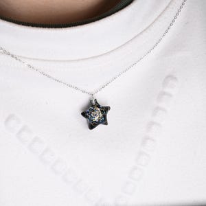 May include: A silver chain necklace with a star-shaped pendant. The pendant is made of black glass with a swirling pattern of gold and white.