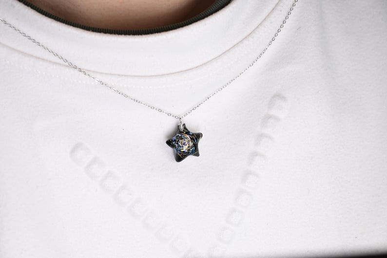 May include: A silver chain necklace with a star-shaped pendant. The pendant is made of black glass with a swirling pattern of gold and white.