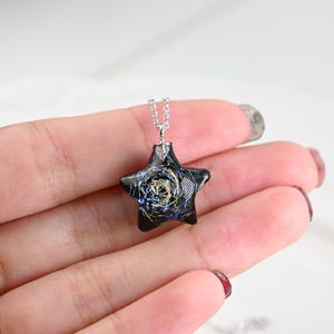 May include: A silver chain necklace with a black star-shaped pendant. The pendant has a swirling pattern of gold and blue glitter inside.