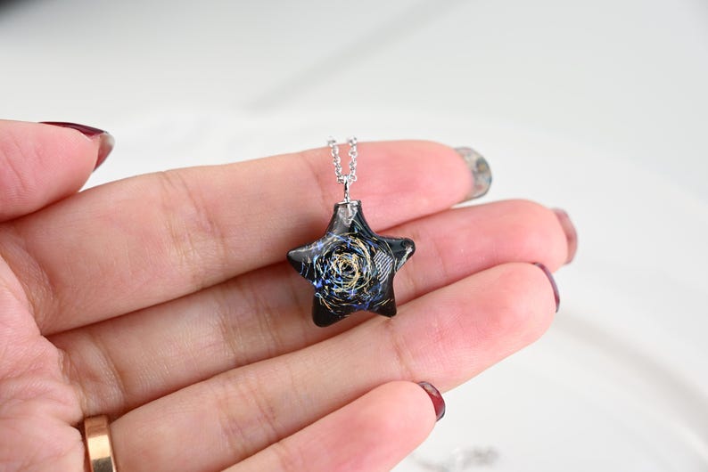 May include: A silver chain necklace with a black star-shaped pendant. The pendant has a swirling pattern of gold and blue glitter inside.