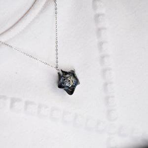 May include: A silver chain necklace with a black star-shaped pendant featuring a galaxy design.