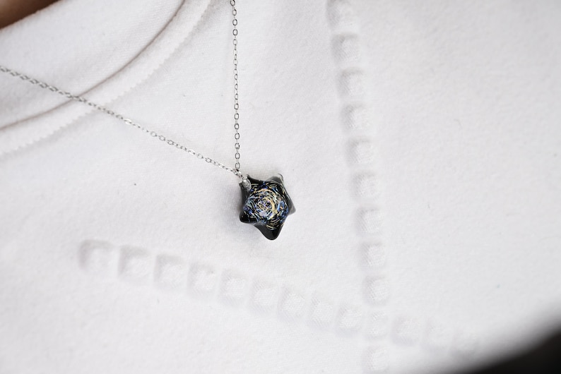 May include: A silver chain necklace with a black star-shaped pendant featuring a galaxy design.