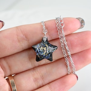 May include: A silver chain necklace with a black star-shaped pendant. The pendant has a blue and gold swirl design.