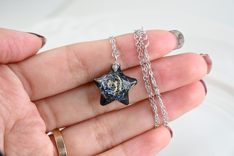 May include: A silver chain necklace with a black star-shaped pendant. The pendant has a blue and gold swirl design.