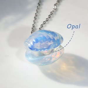 Op de afbeelding: Een zilveren ketting met een blauwe en witte opaal schelp hanger. De hanger is open om een ​​kleinere opaal in de binnenkant te onthullen.