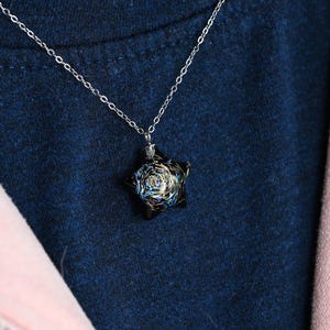 May include: A silver chain necklace with a black star-shaped pendant. The pendant has a swirling, galaxy-like design with blue, white, and gold accents.