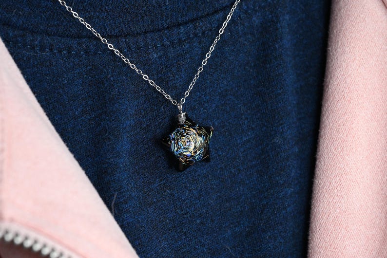 May include: A silver chain necklace with a black star-shaped pendant. The pendant has a swirling, galaxy-like design with blue, white, and gold accents.