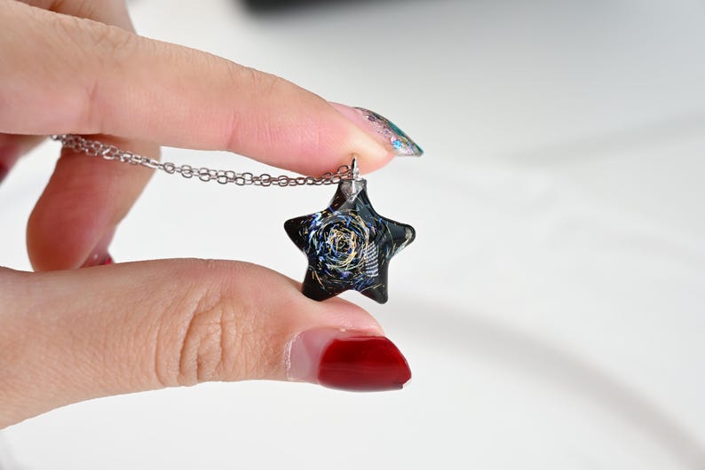 May include: A silver chain necklace with a black star-shaped pendant. The pendant has a swirling, galaxy-like design with gold accents.