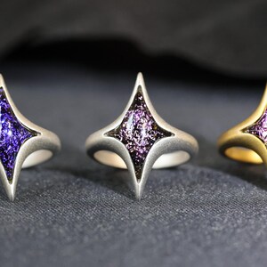 May include: Three rings in silver, gold, and black with a purple star-shaped stone set in the centre.