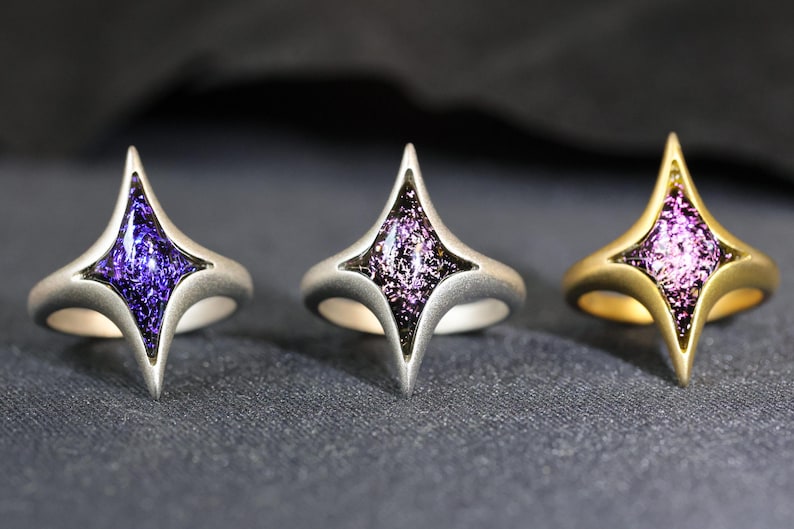 May include: Three rings in silver, gold, and black with a purple star-shaped stone set in the centre.