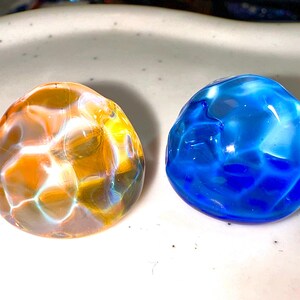 Puede incluir: Dos canicas de vidrio, una es naranja con remolinos blancos y la otra es azul con remolinos blancos.