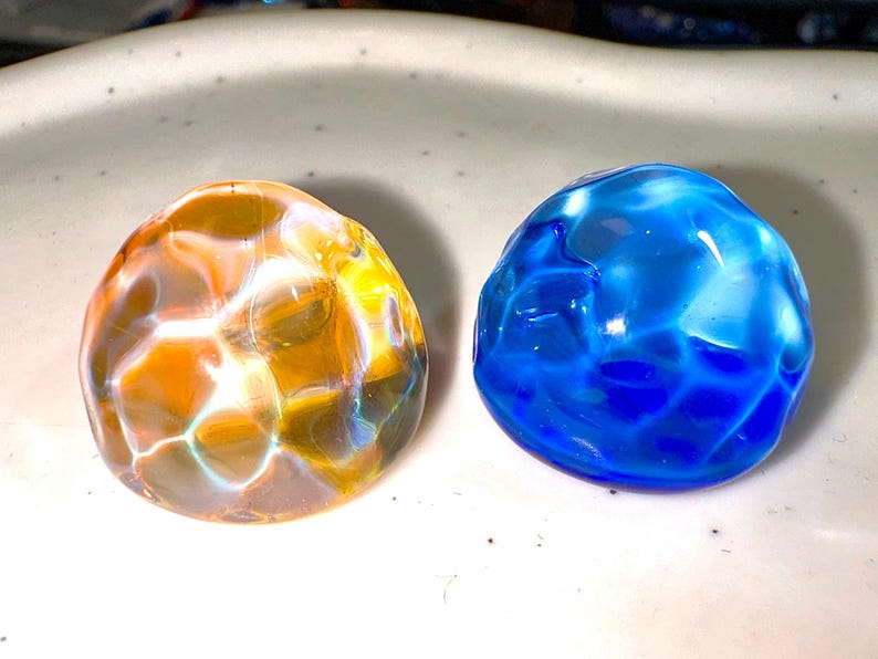 Puede incluir: Dos canicas de vidrio, una es naranja con remolinos blancos y la otra es azul con remolinos blancos.