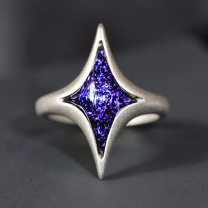 May include: A silver ring featuring a four-pointed star design. The star is set with a purple glass stone.