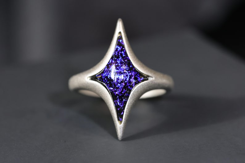 May include: A silver ring featuring a four-pointed star design. The star is set with a purple glass stone.
