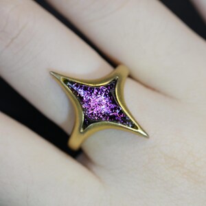 May include: A gold ring featuring a star-shaped stone with a purple, glittery finish.