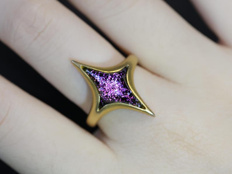 May include: A gold ring featuring a star-shaped stone with a purple, glittery finish.