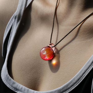 May include: A red glass pendant necklace with a crescent moon design. The pendant is on a brown cord necklace.