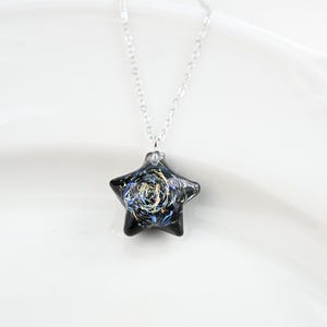 May include: A silver chain necklace with a black star-shaped pendant. The star has a swirling pattern of gold and blue paint.