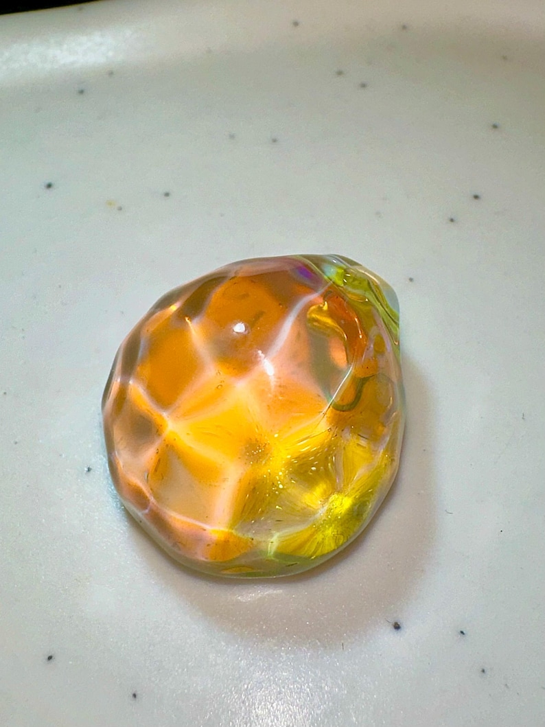 Puede incluir: Una esfera de vidrio transparente y facetada con un brillo iridiscente amarillo y naranja.