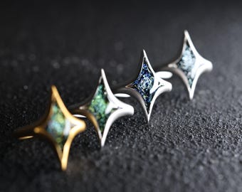 May include: Four silver rings with a star-shaped design. Each ring features a different iridescent glass inlay in shades of blue, green, and gold.