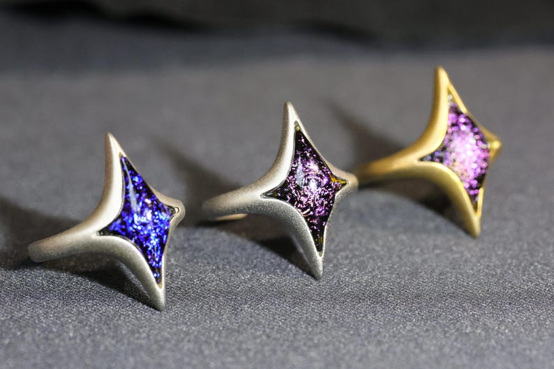 May include: Three silver rings with a star-shaped design. Each ring features a different colour of iridescent glass in the centre of the star: blue, purple, and pink.