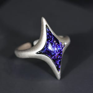 May include: A silver ring featuring a blue, sparkly, geometric gem in the shape of a star.