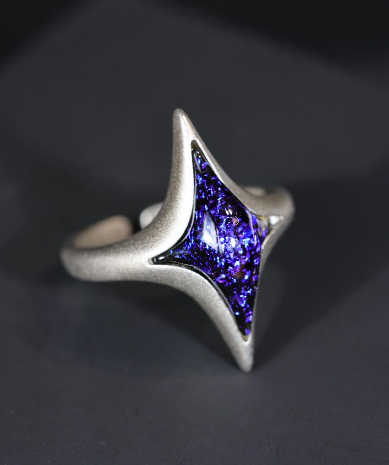 May include: A silver ring featuring a blue, sparkly, geometric gem in the shape of a star.