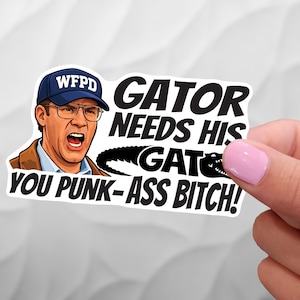 May include: A white sticker featuring a cartoon image of a man wearing a blue cap with "WFPD" on it, glasses, and an open mouth. The sticker has the text "GATOR NEEDS HIS GATOR YOU PUNK-ASS BITCH!" in black.