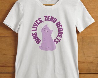 May include: White t-shirt with a purple cat illustration and the text "NINE LIVES, ZERO REGRETS" in a circular design. The cat is looking up with a relaxed expression. The shirt is hanging on a wooden hanger.