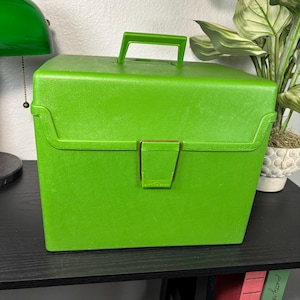 以下が含まれることがあります： 明るい緑色のヴィンテージキャリングケース。持ち手と留め金がマッチしています。長方形のケースは質感のある表面で、黒いテーブルの上に置かれています。ケースは鮮やかな緑色です。