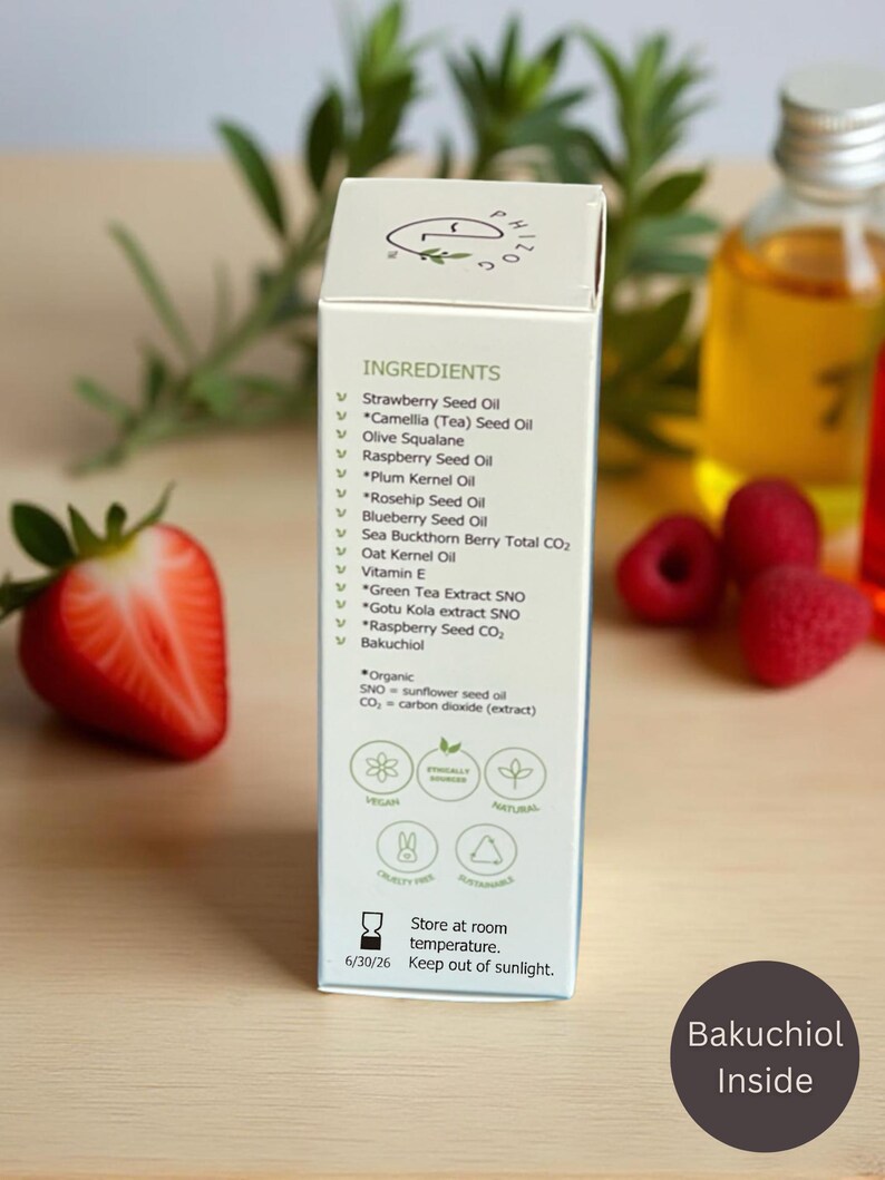 May include: A white product box with the word "INGREDIENTS" and a list of ingredients, including Strawberry Seed Oil and Bakuchiol. The box is next to a cut strawberry and a bottle of oil. The text "Bakuchiol Inside" is on a dark circle.