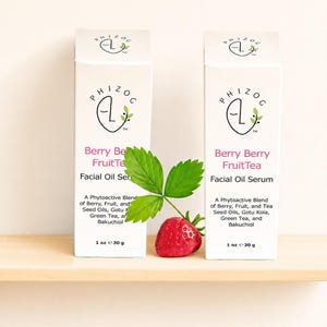 May include: Two white boxes of facial oil serum with the text "Berry Berry FruitTea" and "Facial Oil Serum". A strawberry and green leaf are in front of the boxes. Each box contains 1 oz of product.