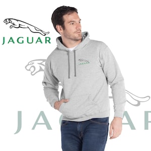 Könnte beinhalten: Ein grauer Kapuzenpullover mit einem kleinen grün-schwarzen Jaguar-Logo auf der linken Brust. Das Logo trägt den Schriftzug "Jaguar" in grüner Schrift.