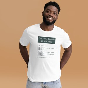 Può includere: Una maglietta bianca con una stampa grafica nera e verde che recita "The Only Comment of the Code" e include un blocco di codice con commenti. Il codice include il testo "Caro manutentore: Quando ho scritto questo codice, solo io e Dio sapevamo cosa faceva. Ora, solo Dio lo sa."