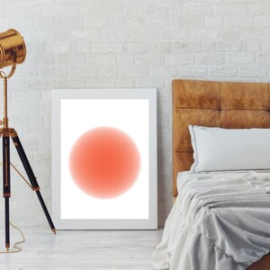 Può includere: Una stampa incorniciata bianca con un unico grande cerchio rosso al centro. Il cerchio ha un effetto sfumato, passando da un rosso più scuro al centro a un rosso più chiaro ai bordi. La stampa è appesa a un muro di mattoni bianchi sopra una testiera in pelle marrone.