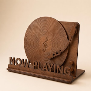 May include: A brown wooden display stand featuring a circular record design with a treble clef symbol in the centre and a tonearm. The base of the stand includes the text NOW PLAYING in bold, cut-out letters, along with two small circular knobs on the side.