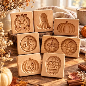 Op de afbeelding: Een verzameling van zeven lichtgekleurde houten koekjesvormen met uitgesneden ontwerpen, waaronder een pompoenkoets, een spook, een pompoen, een heks op een bezemsteel, een pompoen met bladeren, eikels, een pompoenlantaarn en een decoratieve suikerschedel.