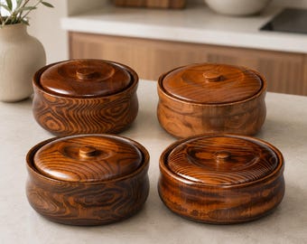 May include: Four round wooden containers with matching lids, each featuring a polished dark brown finish and visible natural wood grain patterns. The containers are arranged in a two-by-two grid, showcasing a smooth, curved exterior design.