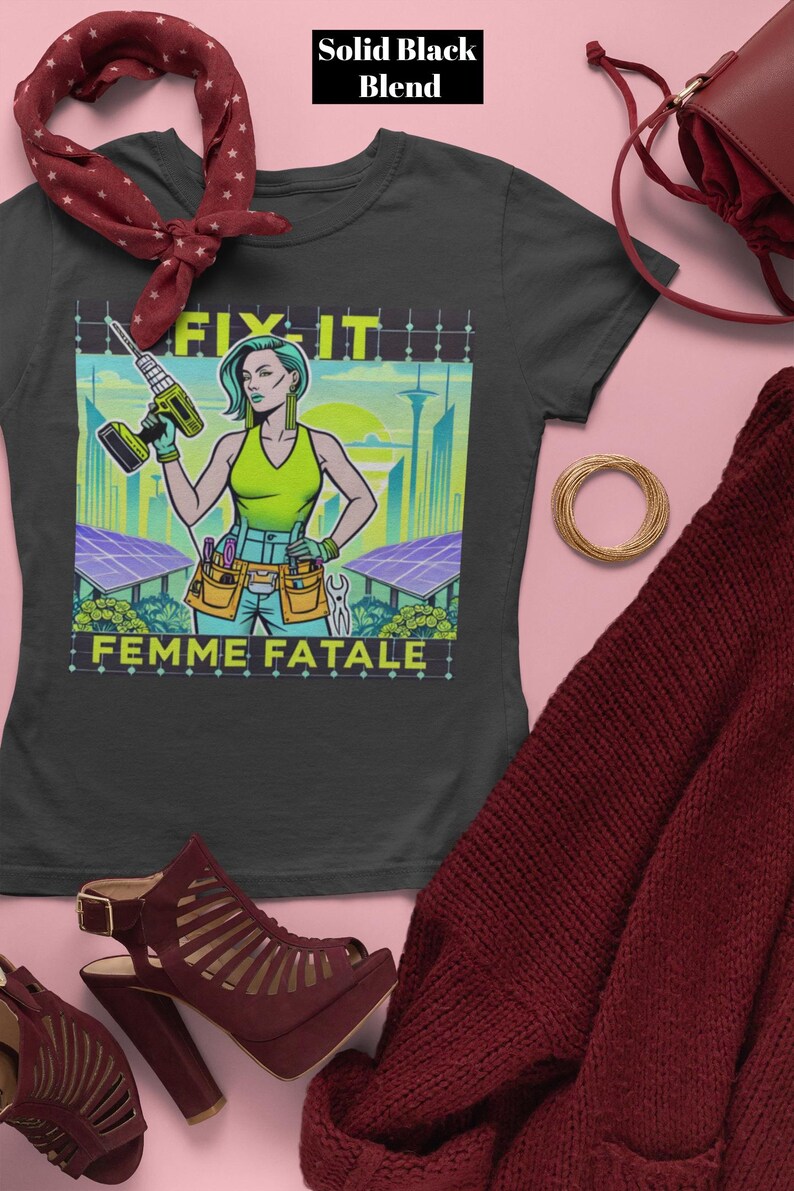 May include: A black t-shirt with a graphic of a woman holding a drill, the words "FIX IT" and "FEMME FATALE". The woman is wearing a green top and tool belt. The background features a cityscape and solar panels.
