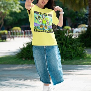 May include: Yellow t-shirt with the text "FIX IT" and "FEMME FATALE" featuring a cartoon woman holding a drill. The woman is wearing a green top and tool belt. The model is wearing a denim skirt and white trainers.