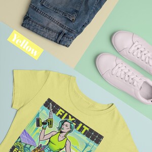 May include: A pale yellow t-shirt featuring a graphic of a woman with a drill, the words "FIX IT" and "FEMME FATALE". The image also includes blue denim shorts and white trainers.