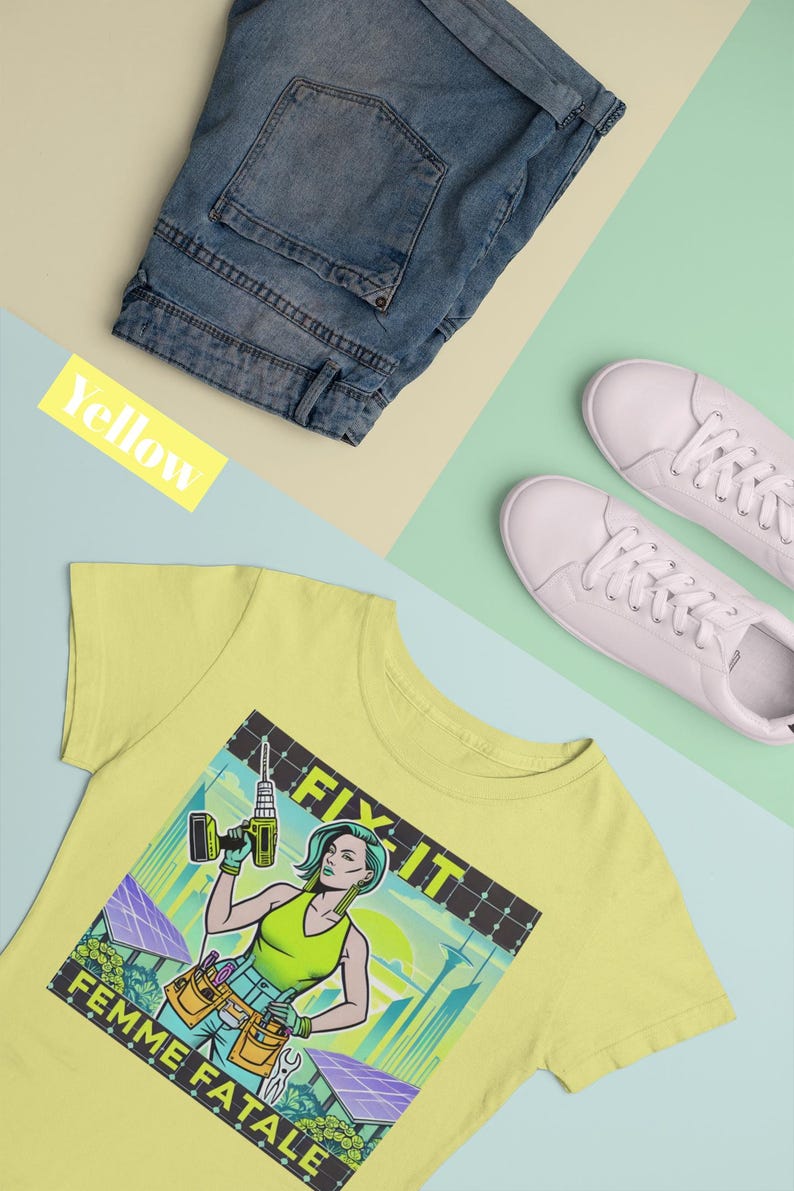 May include: A pale yellow t-shirt featuring a graphic of a woman with a drill, the words "FIX IT" and "FEMME FATALE". The image also includes blue denim shorts and white trainers.