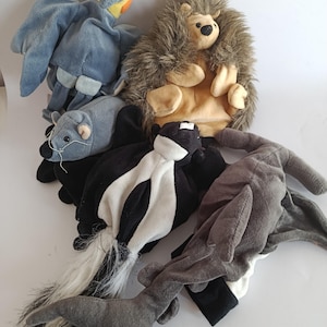 May include: A collection of plush hand puppets in the shapes of various animals. Includes a blue bird, a hedgehog, a skunk, a rat, and a gray animal with a long tail. The puppets are made of soft fabric and are designed to fit over a hand.